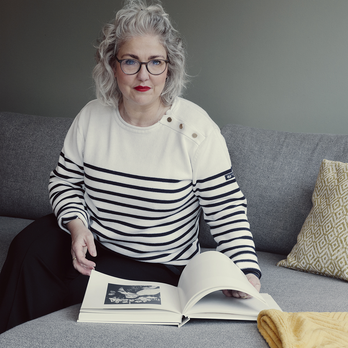 zelfportret van de fotografe Katja Diroen, zittend op een bank met een fotoboek voor zich